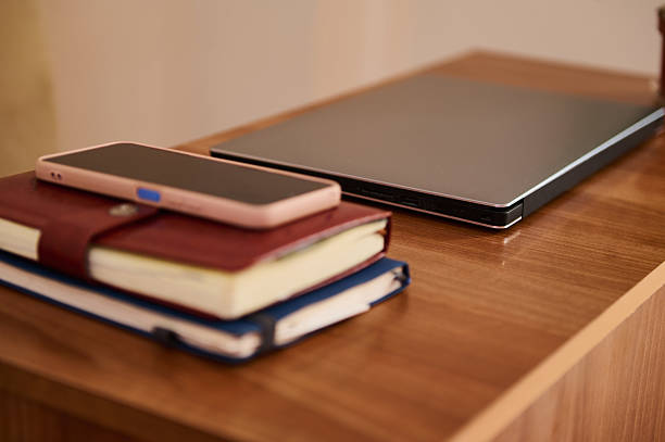 Organized workspace featuring closed laptop, smartphone, and two notebooks on a wooden table. Evoking professionalism and preparation, this setting is perfect for telecommuting or productivity moments