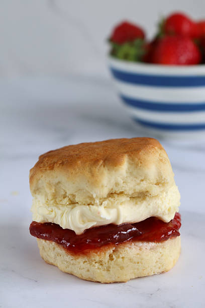 istock Close-up image of plain scone strawberry jam and clotted cream, blue and white striped Cornish ware bowl of strawberries, traditional English afternoon tea topped with jam and cream the Cornish way, white marble effect background, social debate concept 2229994764