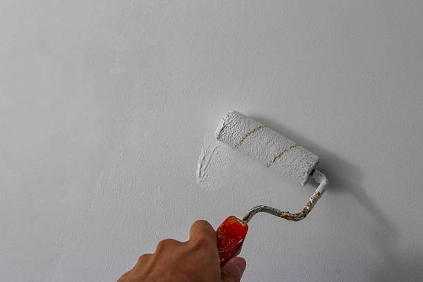 istock Paint roller with orange handle placed against white wall showcasing home improvement and interior decoration tools 2229995014