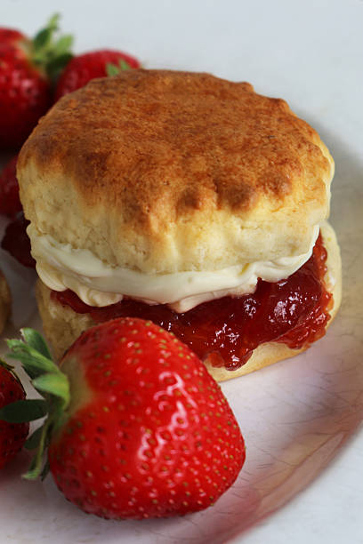 istock Full frame image of individual plain scone with strawberry jam and clotted cream and strawberries on white plate, traditional English afternoon tea, baked good topped with jam and cream the Cornish way, white marble effect background, elevated view 2229995984