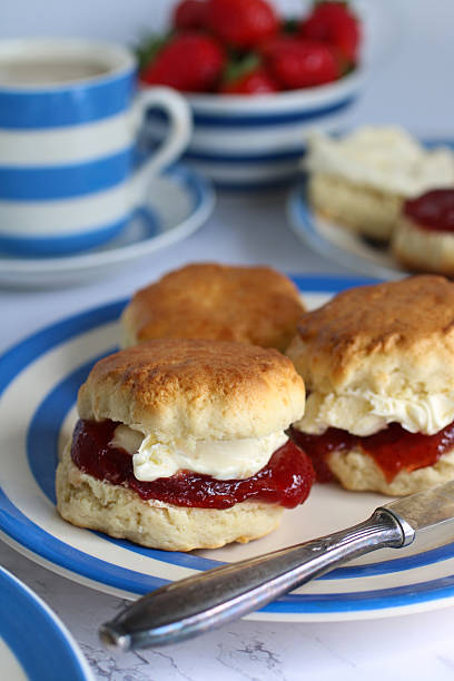istock Image of plain scones with clotted cream and strawberry jam on blue and white striped Cornish ware plate, bowl of strawberries, ramekin of clotted cream, teacup and saucer, traditional English afternoon tea topped with jam and cream the Cornish way 2229999934