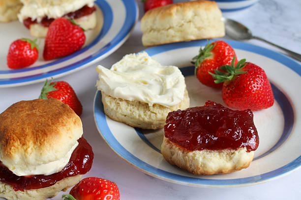 istock Image of plain scones with clotted cream and strawberry jam on blue and white striped Cornish ware plate, bowl of strawberries, teaspoon, traditional English afternoon tea topped with jam and cream in the Cornish way, social debate concept 2230001239