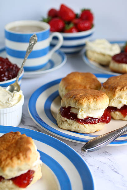 istock Image of plain scones with clotted cream and strawberry jam on blue and white striped Cornish ware plate, bowl of strawberries, ramekin of clotted cream, teacup and saucer, traditional English afternoon tea topped with jam and cream the Cornish way 2230001570