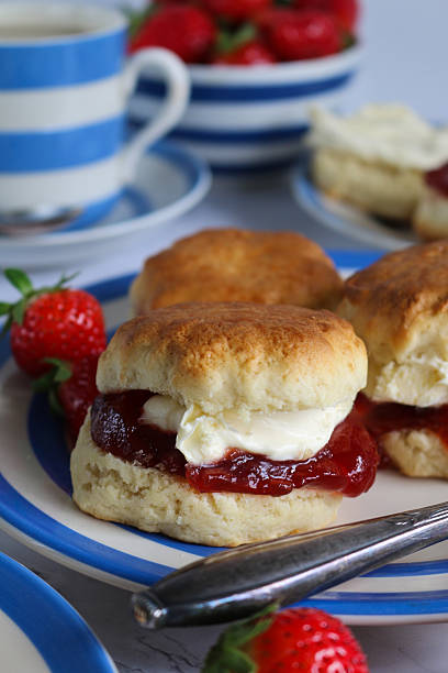 istock Image of plain scones with clotted cream and strawberry jam on blue and white striped Cornish ware plate, bowl of strawberries, ramekin of clotted cream, teacup and saucer, traditional English afternoon tea topped with jam and cream the Cornish way 2230001646
