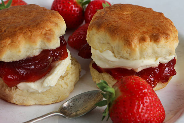 istock Full frame image of plain scones with strawberry jam and clotted cream on white plate with strawberries, metal teaspoon, traditional English afternoon tea topped with jam and cream in the Cornish and Devonshire ways, elevated view,  social debate concept 2230001697