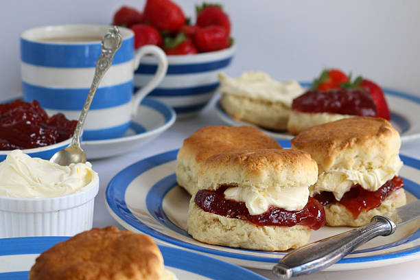 istock Image of plain scones with clotted cream and strawberry jam on blue and white striped Cornish ware plate, bowl of strawberries, ramekin of clotted cream, teacup and saucer, traditional English afternoon tea topped with jam and cream the Cornish way 2230002261