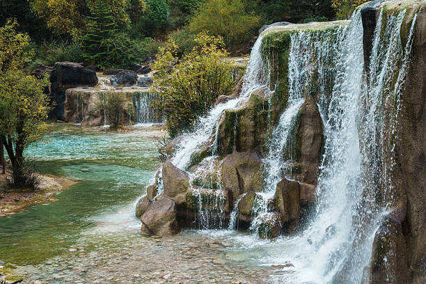 Close-up view of a waterfall flowing into clear emerald water, surrounded by rocks and trees in Blue Moon Valley, Lijiang.