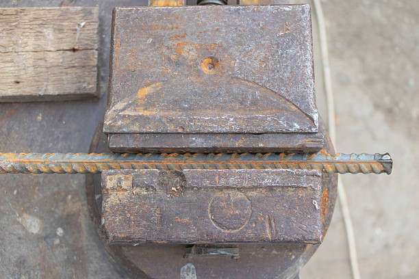 Rusty Metal Vise Holding Ribbed Steel Rebar in Workshop Setting.