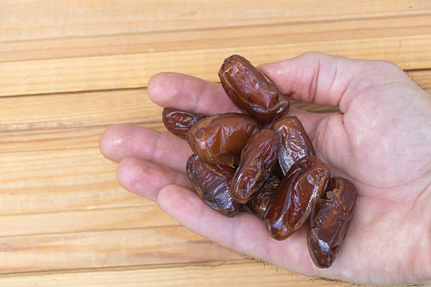 istock Fresh Brown Dates in a Hand on Wooden Surface 2230038723