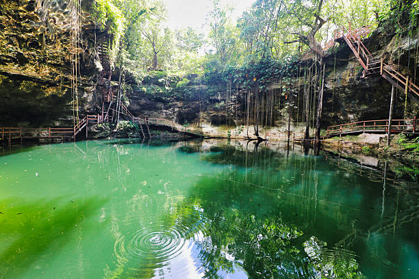 Young, white, caucasian, male man standing on wooden pier in natural pool, cave, cenote Hubiku, illuminated by light, sunbeam from above, close to Valladolid, Mexico