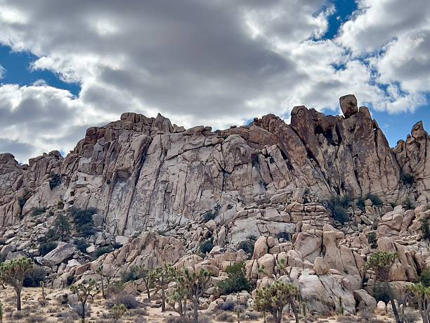Big Mountain Rocks in a desert area with some cactus trees down at the bottom. Blue sky with some white clouds.