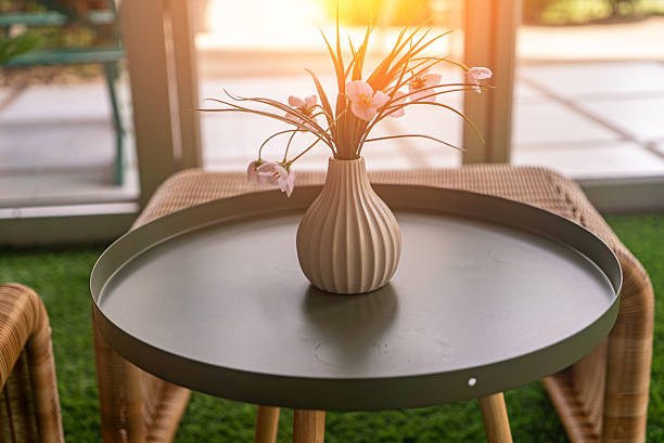 A stylish round table features a decorative vase filled with delicate flowers, set in a bright, modern living space. Sunlight enhances the peaceful ambiance.