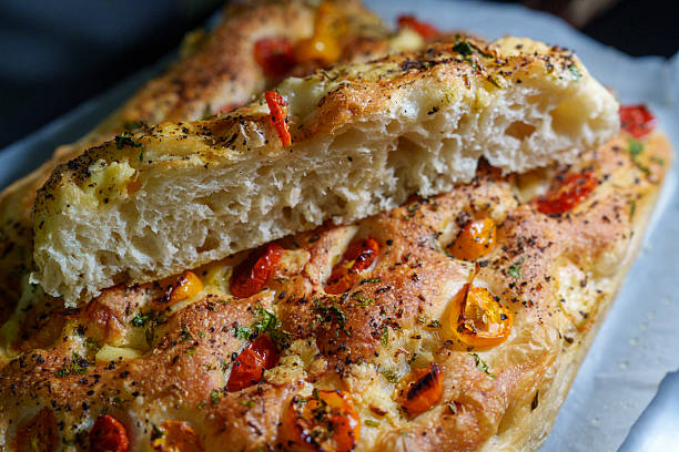 Close-up of freshly baked focaccia bread topped with cherry tomatoes and herbs, sliced to reveal its airy texture and golden crust.
