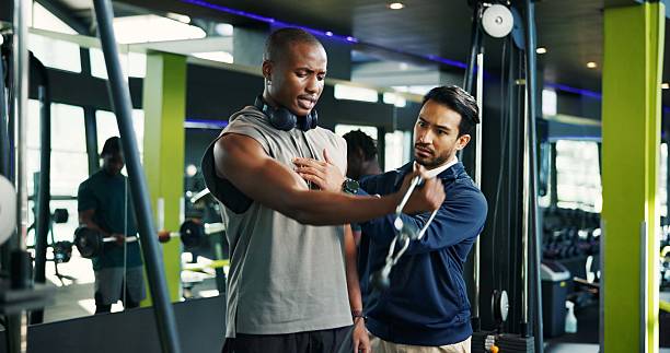 istock Coach, teaching and man with cable machine, exercise and support in bodybuilding. Personal trainer, advice or athlete in training with gym equipment for muscle, power and workout for fitness tips 2230051161