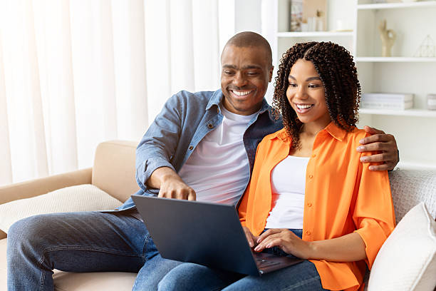 istock Happy young black couple sitting on couch at home, using laptop together 2230056909