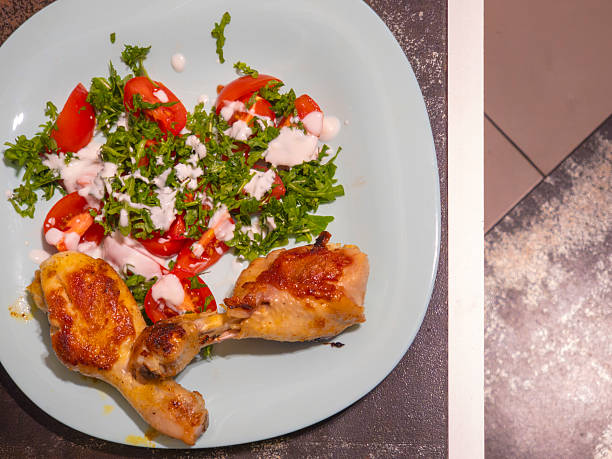 Two roasted chicken legs are served on a light blue plate with a fresh salad of arugula, cherry tomatoes and a creamy dressing, offering a healthy and delicious meal