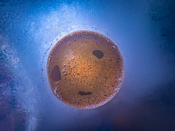 Coffee cup seen from below with condensation forming on glass creating a blue and purple background with bubbles and foam visible in coffee