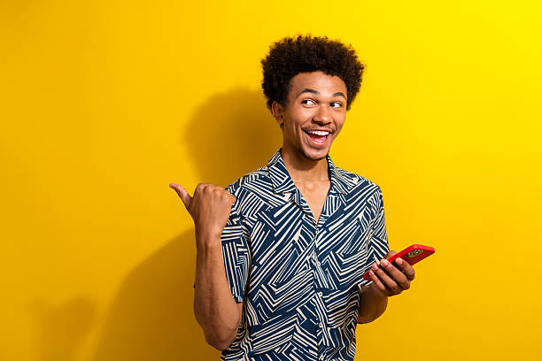 istock Stylish young man posing with smartphone against vibrant yellow background expressing excitement and positivity 2230064393