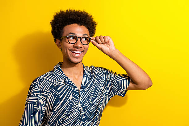 istock Cheerful young man wearing stylish patterned shirt posing with glasses against a bright yellow background 2230064423