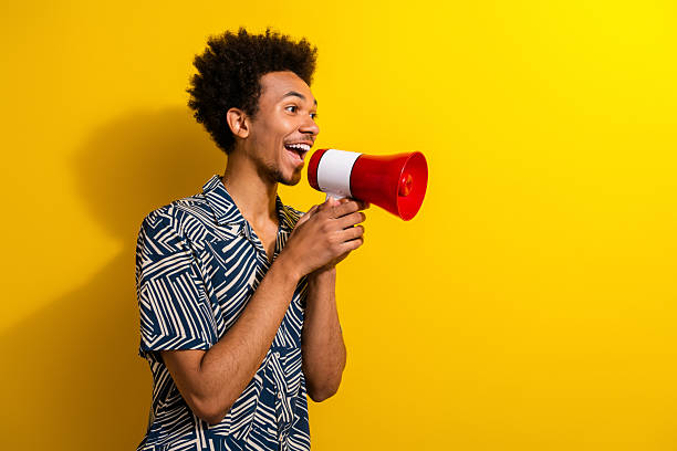 istock Young attractive man holding a megaphone against a bright yellow background, expressing enthusiasm and excitement with a vibrant smile. 2230064458