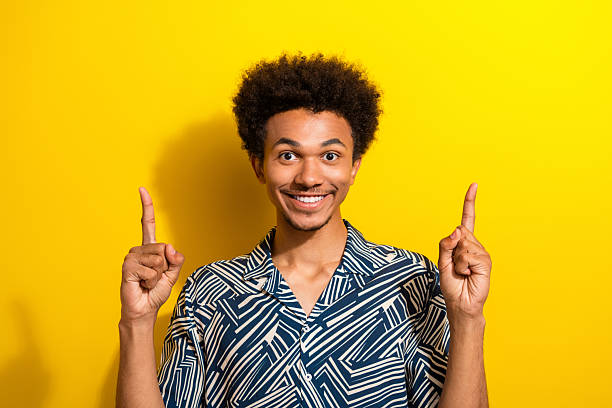 istock Cheerful young man gesturing with raised hands on vibrant yellow background, expressing excitement and happiness in casual style 2230064554