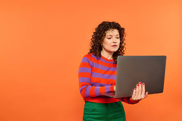 istock Young woman expresses vibrant emotions while working on a laptop in a lively orange setting 2230069825
