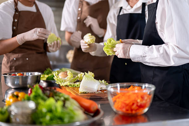 istock Close up of chef and her assistants separating cabbage leaves while standing around kitchen counter. 2230071698
