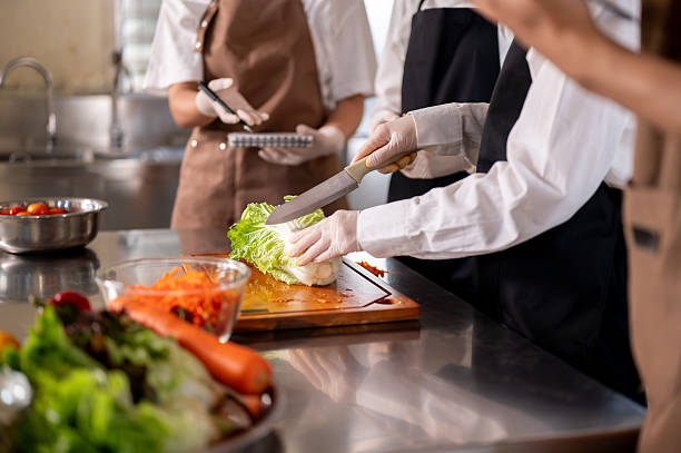 istock Chef holding knife cutting cabbage on chopping board with students or assistants at kitchen counter 2230071771
