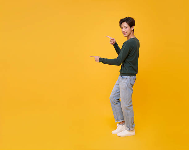 istock Copy space choice concept cheerful Asian man presenting pointing finger on yellow background for ad banner, product mockup, decision making, and marketing design. 2230073045