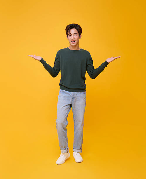 istock Copy space choice concept cheerful Asian man presenting two options with open palms on yellow background for ad banner, product mockup, decision making, and marketing design. 2230073049