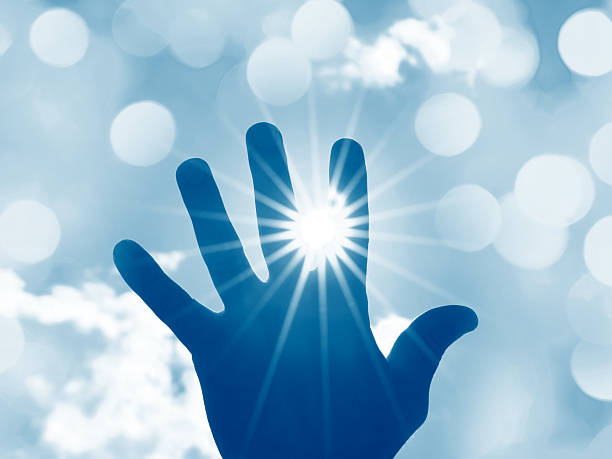 Male hand trying to reach the sun with beautiful sunbeams in the sky with light clouds and bokeh lights. Toned image, space for copy.