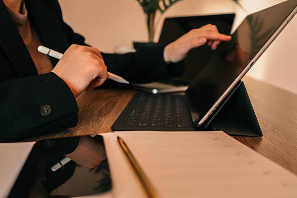 istock Person working on tablet with keyboard case at desk, holding stylus, with smartphone, notebook, and pen in modern office setting 2230074246