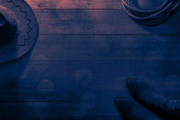 Cowboy hat, boots and lasso on barn wood texture background with beautiful bokeh. American wild west concept. Can be used as a template with space for copy.