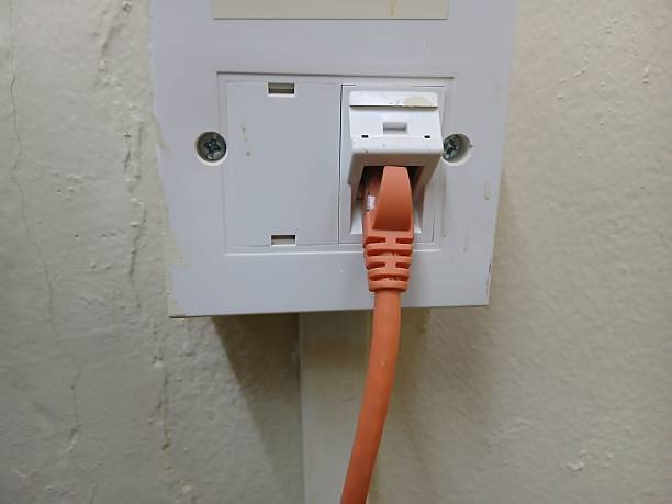 istock Orange internet cable in a white electrical outlet on a yellow wall 2230082626