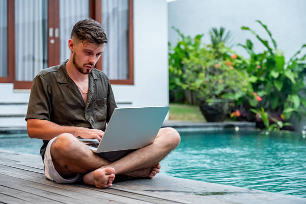 istock Man Using Laptop by the Poolside in a Relaxing Setting 2230084173