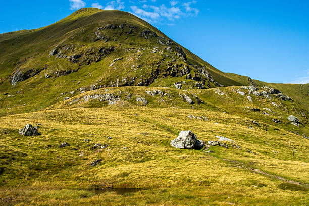 The peak of the highest mountain in Breadalbane region - Ben Lawers in Scottish Highlands, rocks and green grass, blue sky of a hot summer day