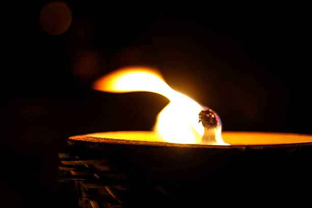 Close-up shot of hand holding a glowing candle, gently lighting a flame in a traditional oil lamp at a sacred shrine. The flicker of light symbolizes spiritual intention, inner peace, and the act of offering light to the divine. Rooted in cultural reverence and mu-te-lu belief, this serene ritual reflects a growing trend toward mindful practices, energy cleansing, and spiritual wellness