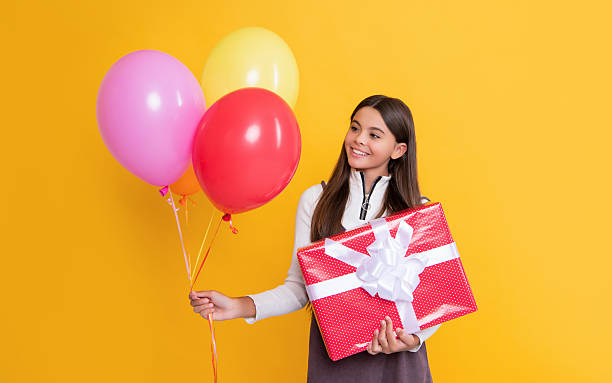istock child smile with party helium balloons and present box on yellow background 2230092995