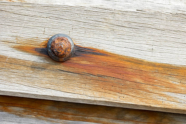 A detailed view of an oxidized iron bolt embedded in weathered wood, displaying rich textures and warm tones from rust staining the surface, highlighting decay and natural aging.