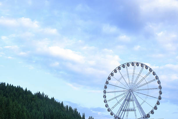 White Ferris wheel towering over lush green forest with mountain backdrop under a deep blue sky, scenic summer travel and eco-tourism destination.
