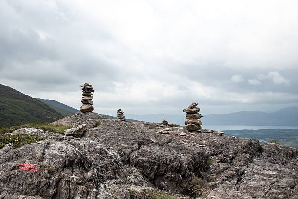 In a rugged landscape, three carefully balanced stone stacks rise above a rocky terrain under a cloudy sky
