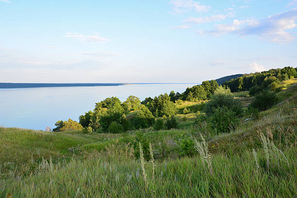 Serene lakeside vista with rolling hills and lush greenery under a sunset sky nature background