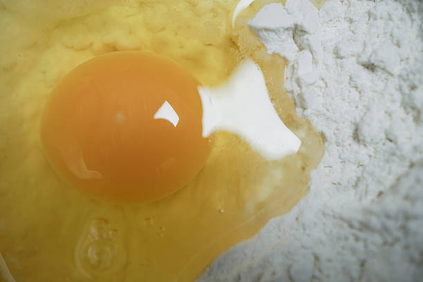 Close up of raw egg with bright yellow yolk sits next to pile of white flour, ready for baking. image captures smooth texture of yolk and powdery surface of flour