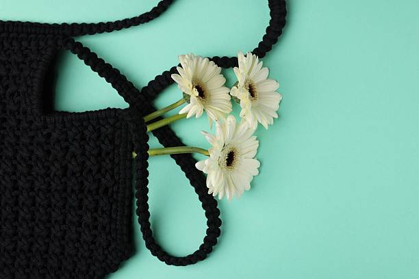 Macrame shopping bag with beautiful flowers on turquoise background, top view. Space for text