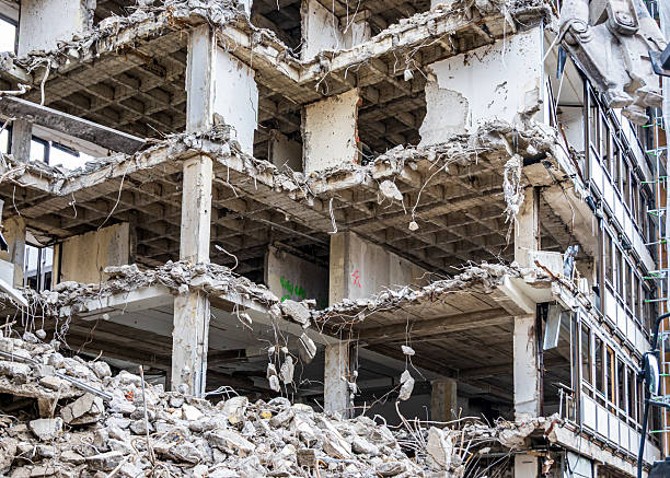 Crumbling concrete remnants of a once tall structure create a chaotic landscape filled with debris, showcasing the impact of demolition or natural disaster in a city setting.