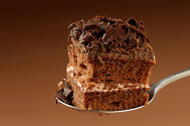A close up shot of a hand offering a slice of chocolate cake.