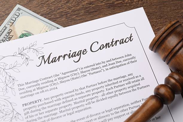 Marriage contract, gavel and dollar bill on wooden table, top view