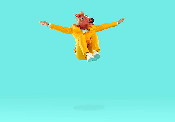 Man with dinosaur head jumping in air on yellow background. Funny man in yellow suit jumping high with his arms outstretched. Freedom, eccentricity, success concept
