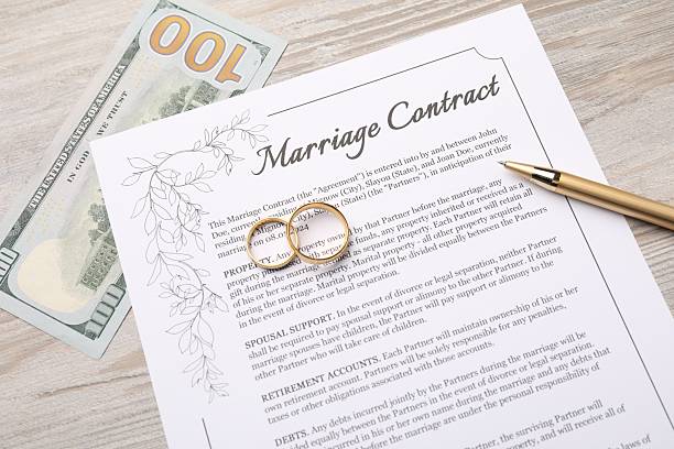 Marriage contract, pen, dollar bill and golden rings on light wooden table, top view