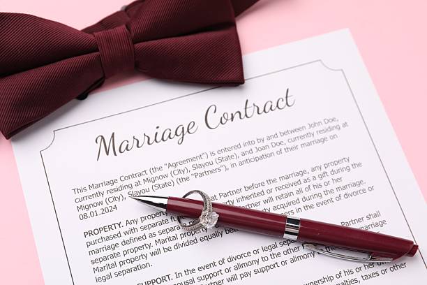 Marriage contract, bowtie, pen and ring on pink background, above view